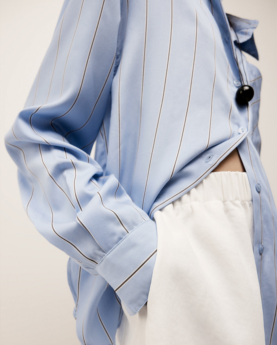 Light blue pinstripe shirt with a black necklace on a neutral background