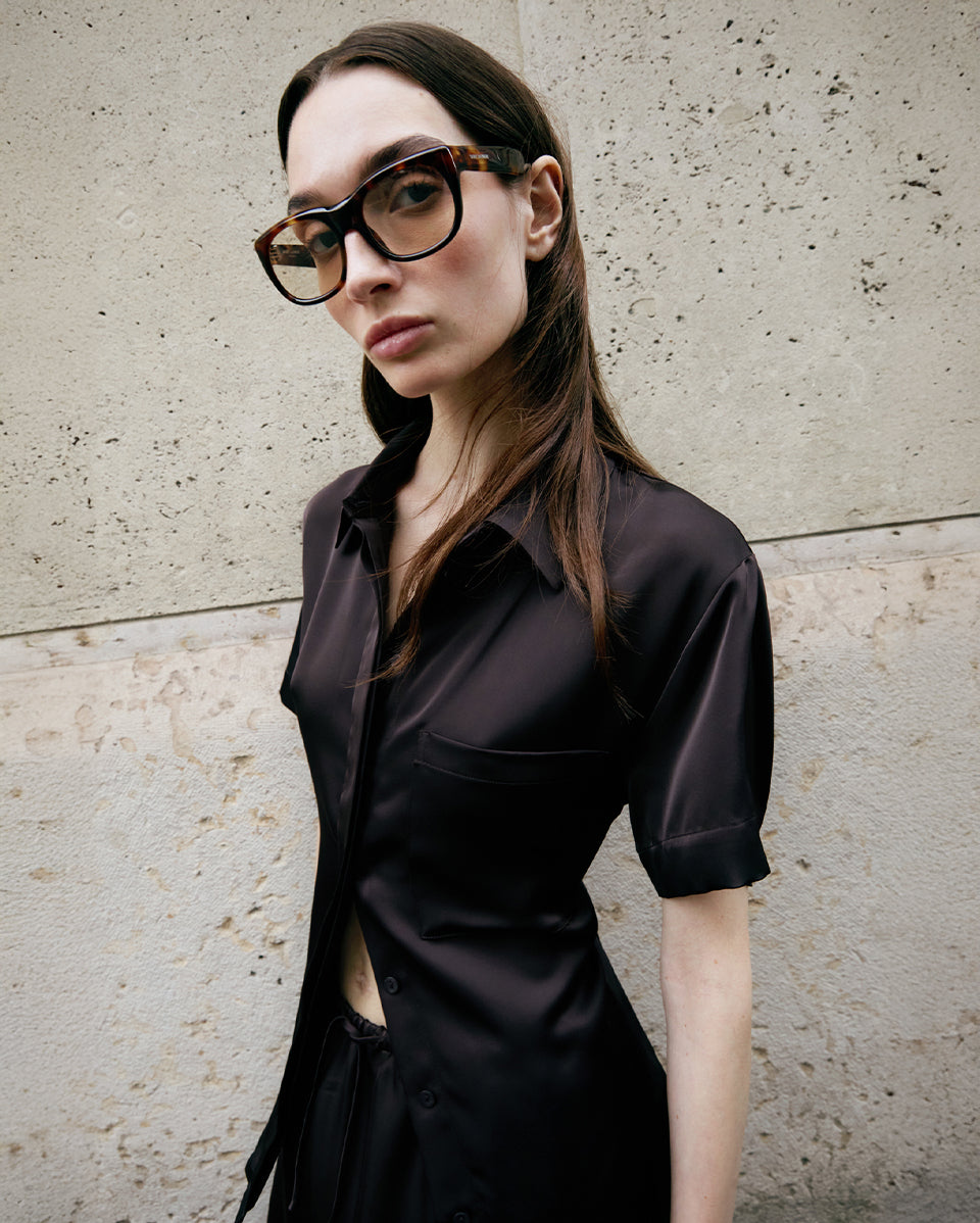 Woman wearing a brown outfit and glasses against a concrete wall