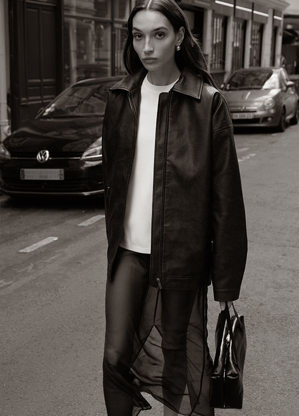 Woman walking on a city street wearing a black leather jacket and sheer black skirt.
