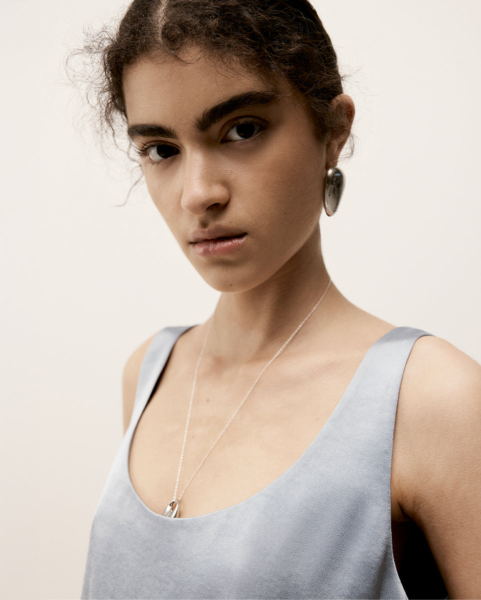 Woman wearing a light blue tank top and a necklace with a plain background