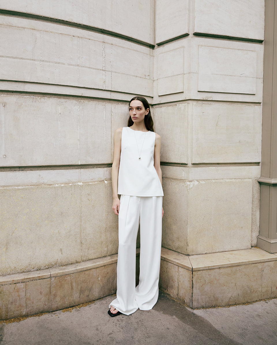 Woman in a white outfit standing against a light-colored wall.