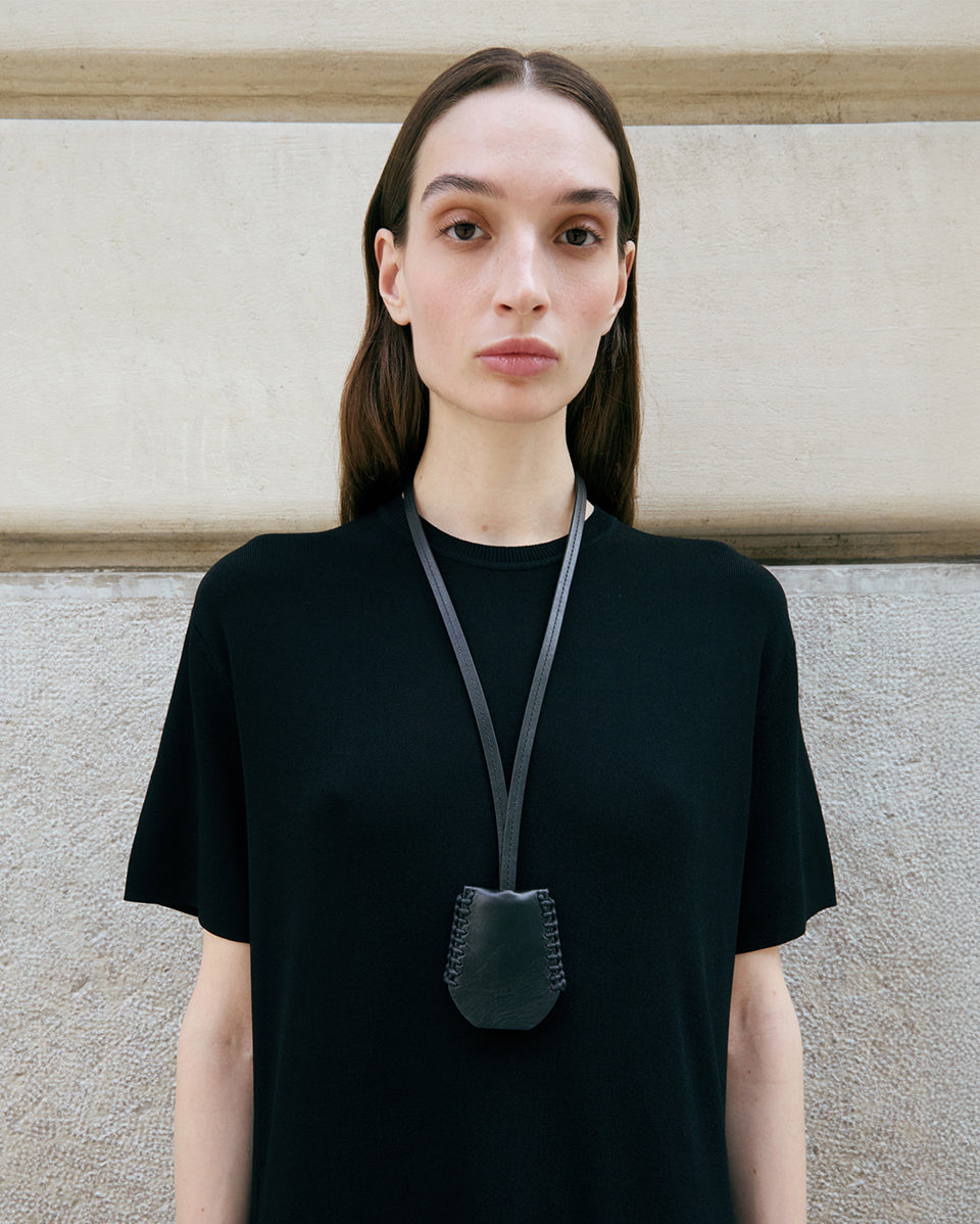 Person wearing a black t-shirt with a leather pouch around their neck against a neutral background